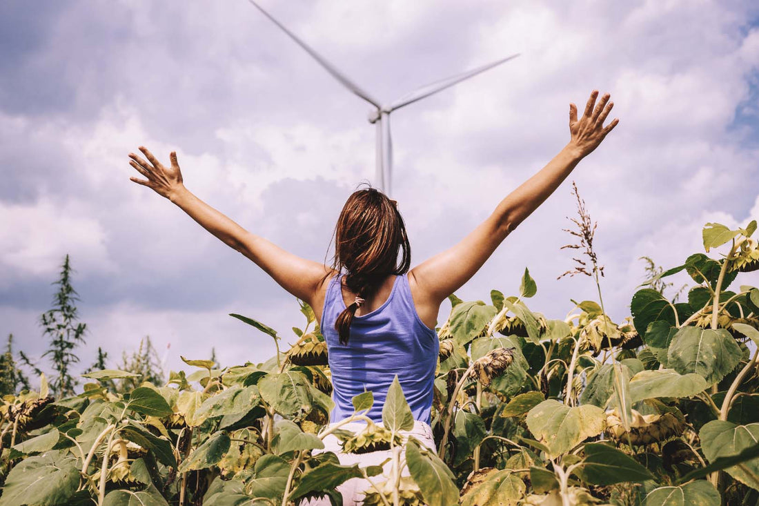 Frau breitet die Arme vor einem Windrad aus, während sie in einem Feld steht