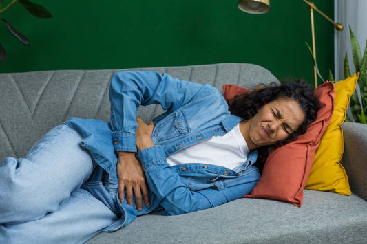 Frau mit Schmerzen in der Bauchgegend auf dem Sofa liegend
