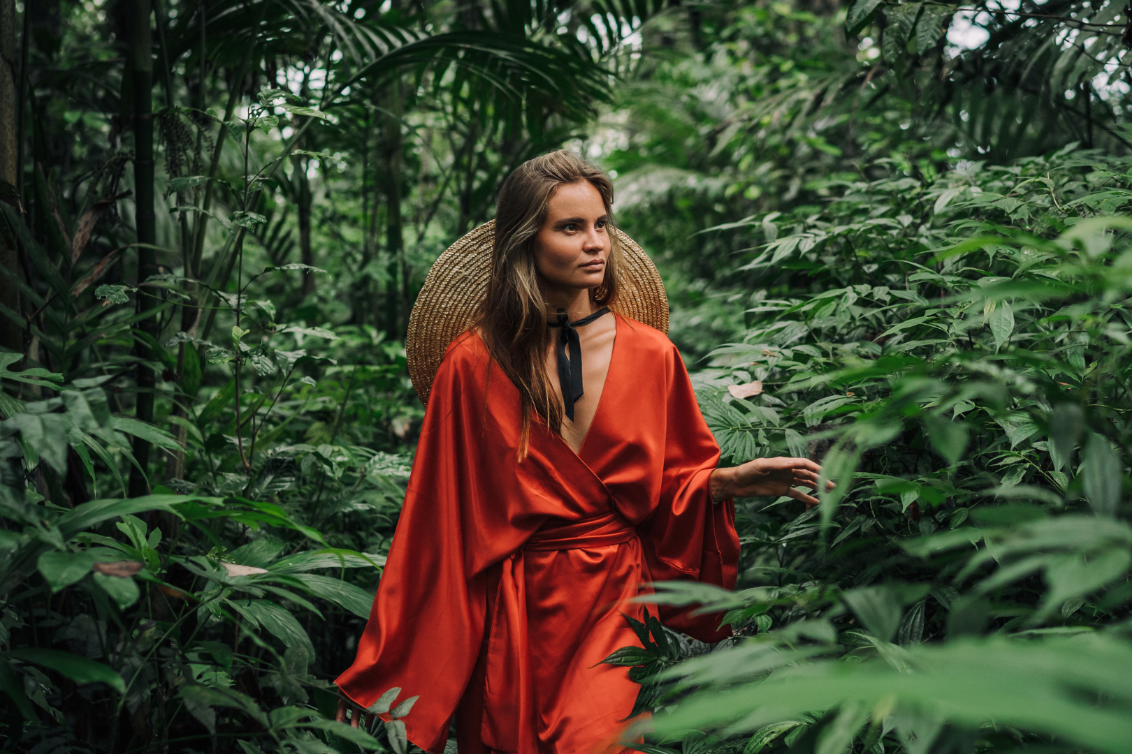 Frau in rotem Kimono aus Baumwollsatin im Dschungel sieht sich um