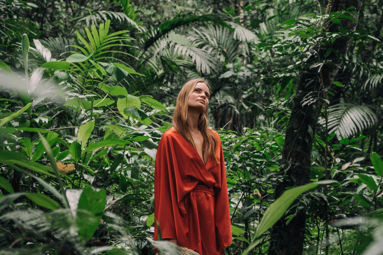Frau in rotem Kimono aus Baumwollsatin im Dschungel schaut in den Himmel