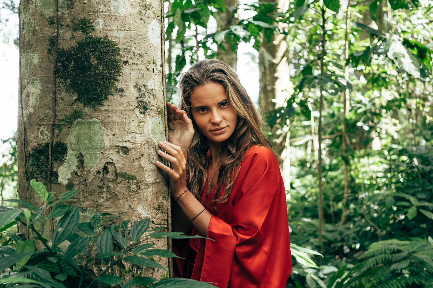 Frau in rotem Kimono aus Baumwollsatin im Dschungel an einen Baum gelehnt