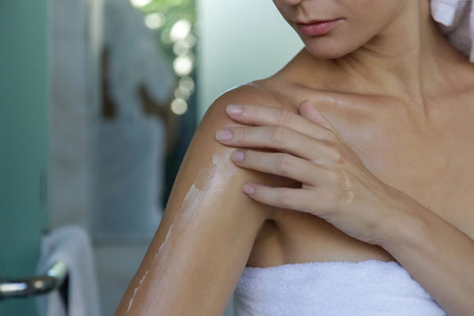 Eine Frau cremt ihren Oberarm im Badezimmer nach dem Duschen ein