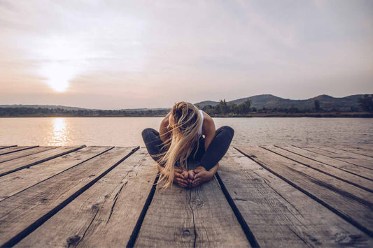 Frau macht Yoga auf einem Holzsteg beim Sonnenuntergang
