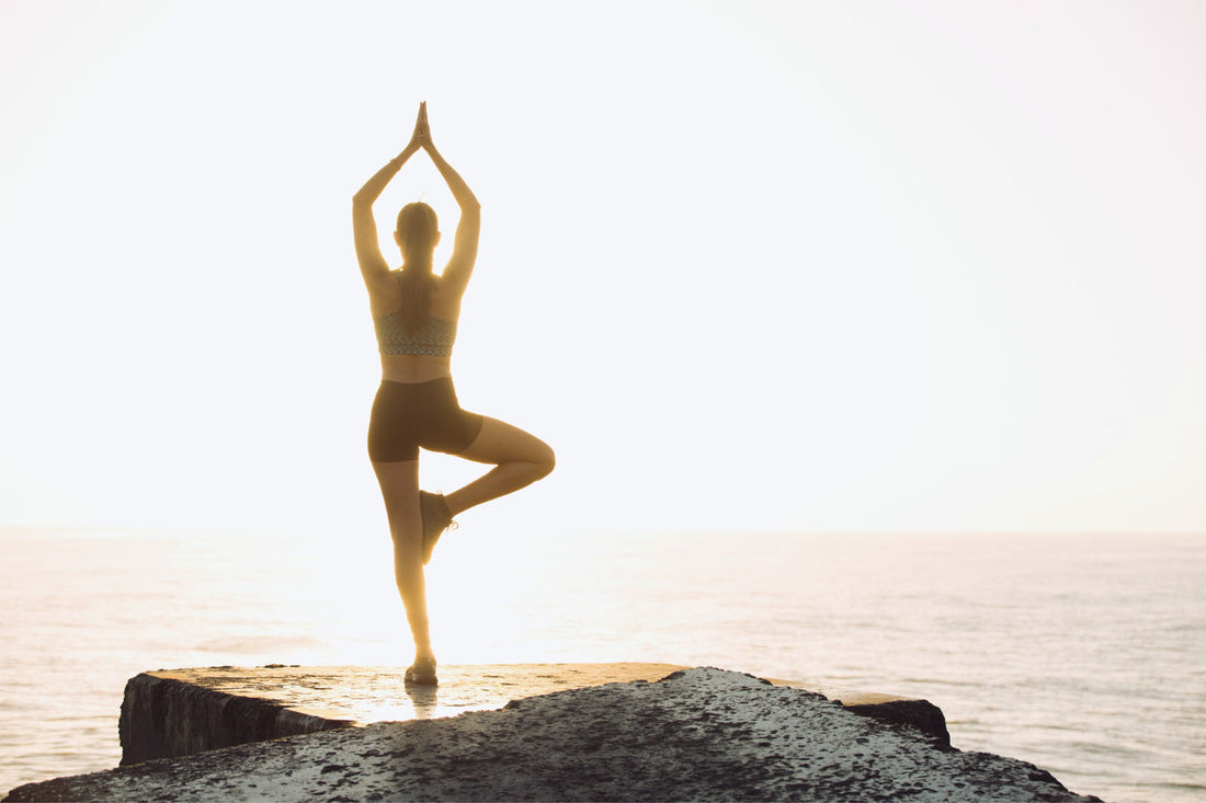 Eine Frau macht Yoga auf einem großen Felsen vor dem Meer