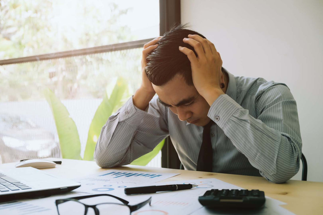 Quite Quitting: Mann gestresst am Arbeitsplatz mit den Händen am gesenkten Kopf