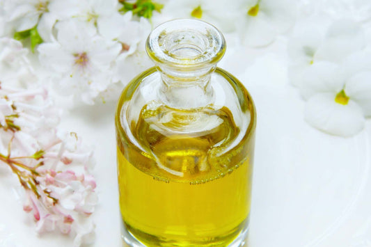 Ölflasche mit gelblichem Öl und dekorativen weißen Blumen drumherum