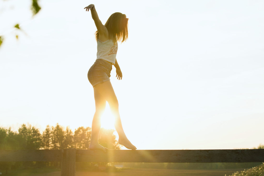 Frau balanciert auf einem Holzbalken in freier Natur beim Sonnenuntergang